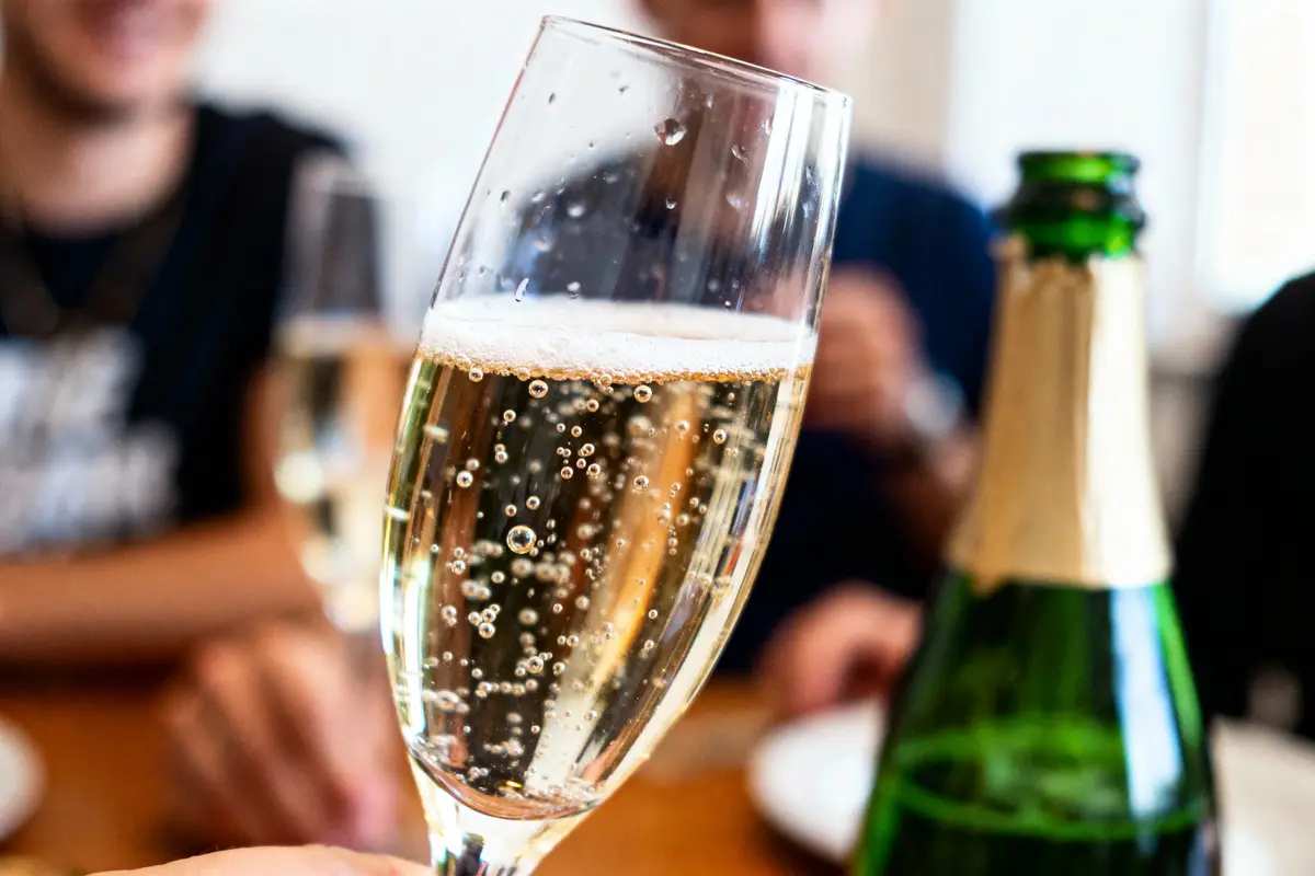 Flûte de champagne pétillant avec bouteille, entourée de personnes floues en arrière-plan lors d'une célébration.