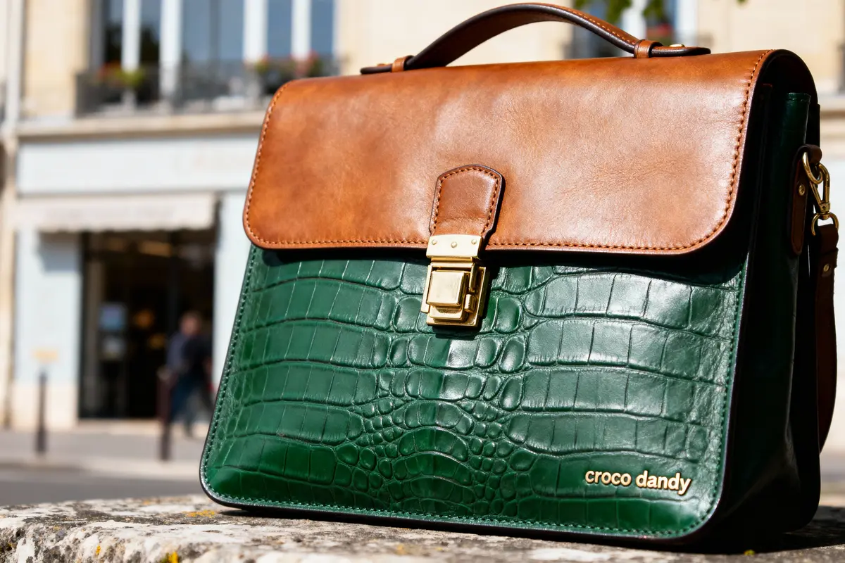 Sac en cuir vert et marron, motif croco, avec fermoir doré, arrière-plan flou urbain.