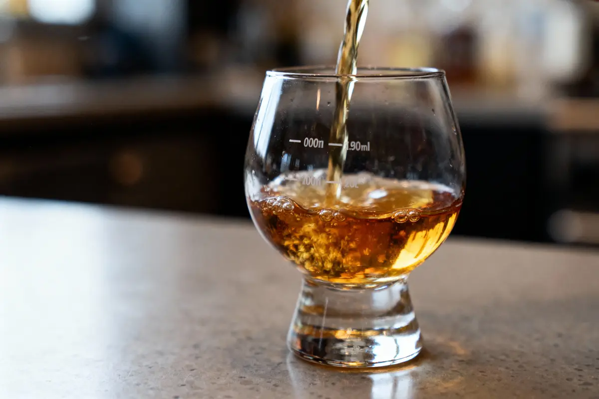 Verre en train d'être rempli de whisky sur un comptoir, avec un fond flou de bar.