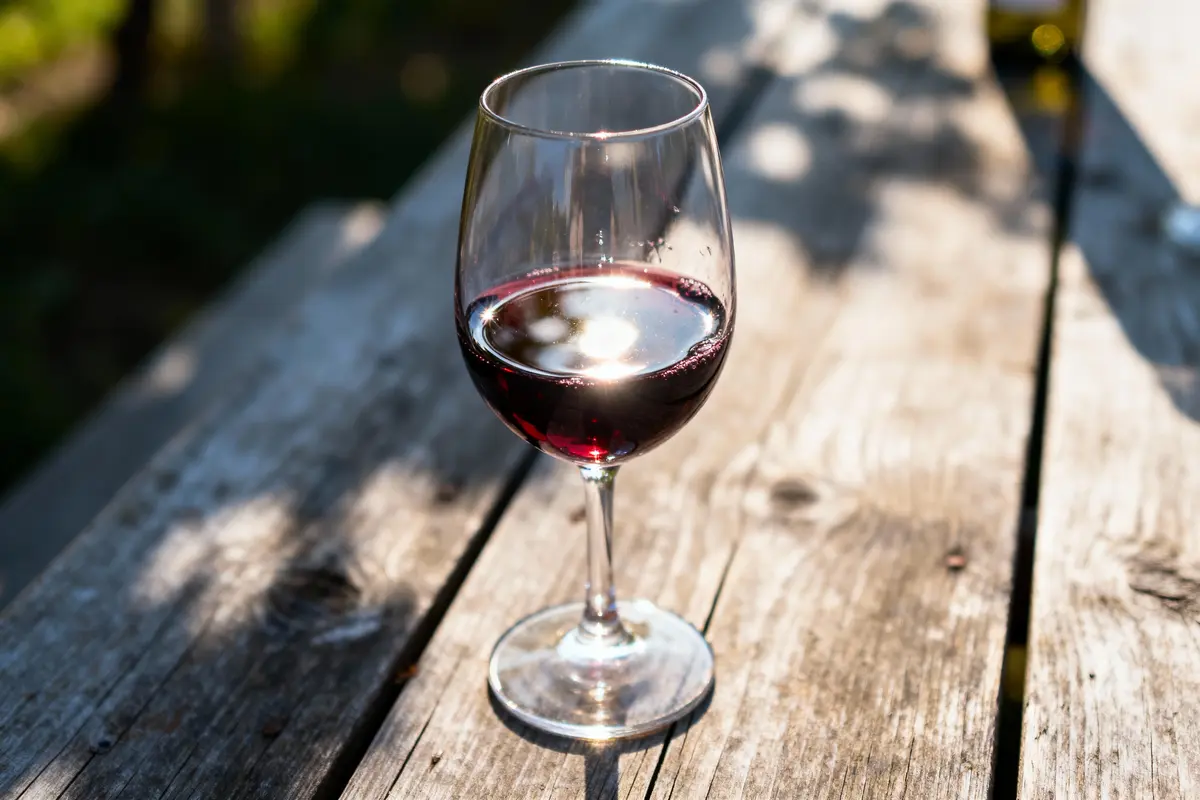 Verre de vin rouge sur une table en bois à l'extérieur, ensoleillée, ombre visible.