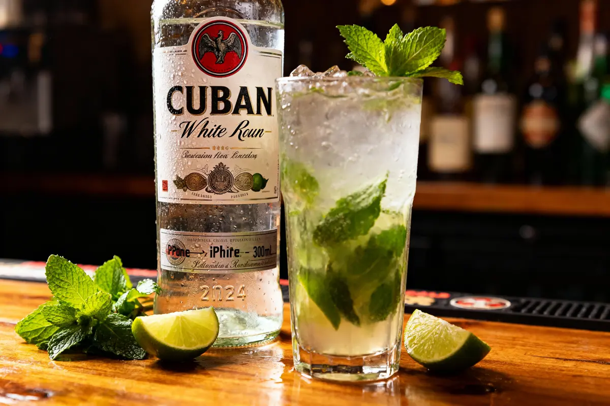 Bouteille de rhum cubain, cocktail mojito, menthe fraîche et rondelles de citron vert sur un bar en bois.
