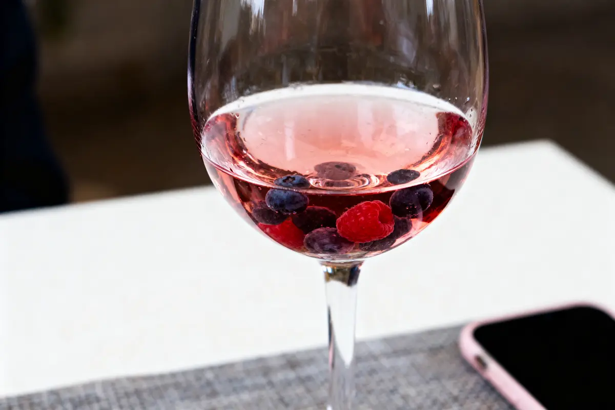 Verre de vin rosé avec framboises et myrtilles, téléphone sur table blanche.