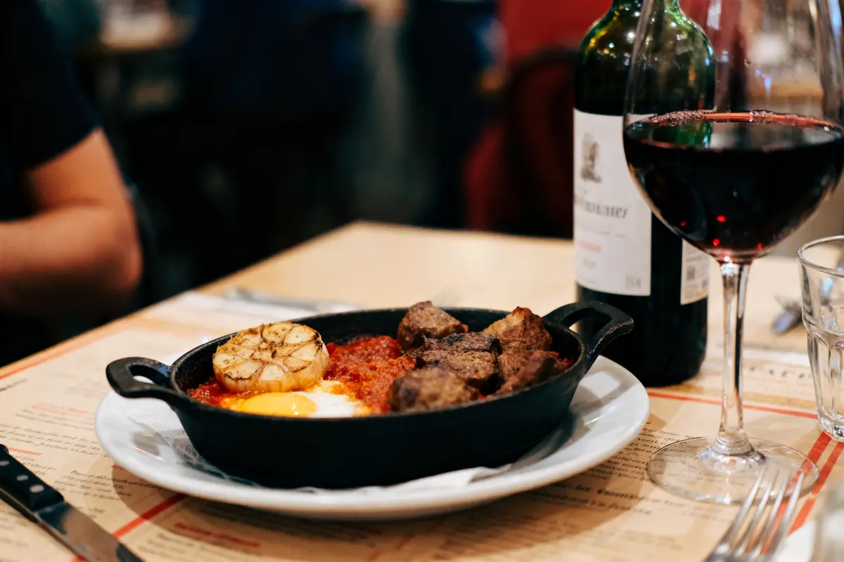 Plat en poêle avec viande, sauce tomate, œuf. Accompagné d'un verre et bouteille de vin rouge.