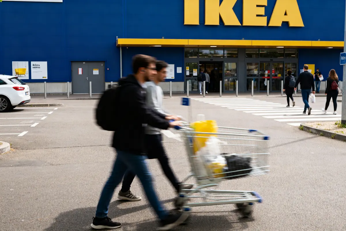 Devant un magasin Ikea, deux personnes poussent un chariot dans le parking.