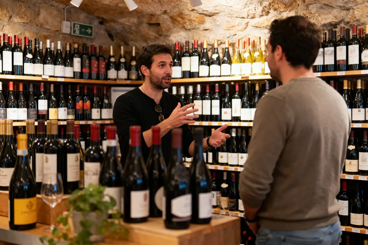 Deux hommes discutant dans un magasin de vin, entourés de nombreuses bouteilles sur les étagères.