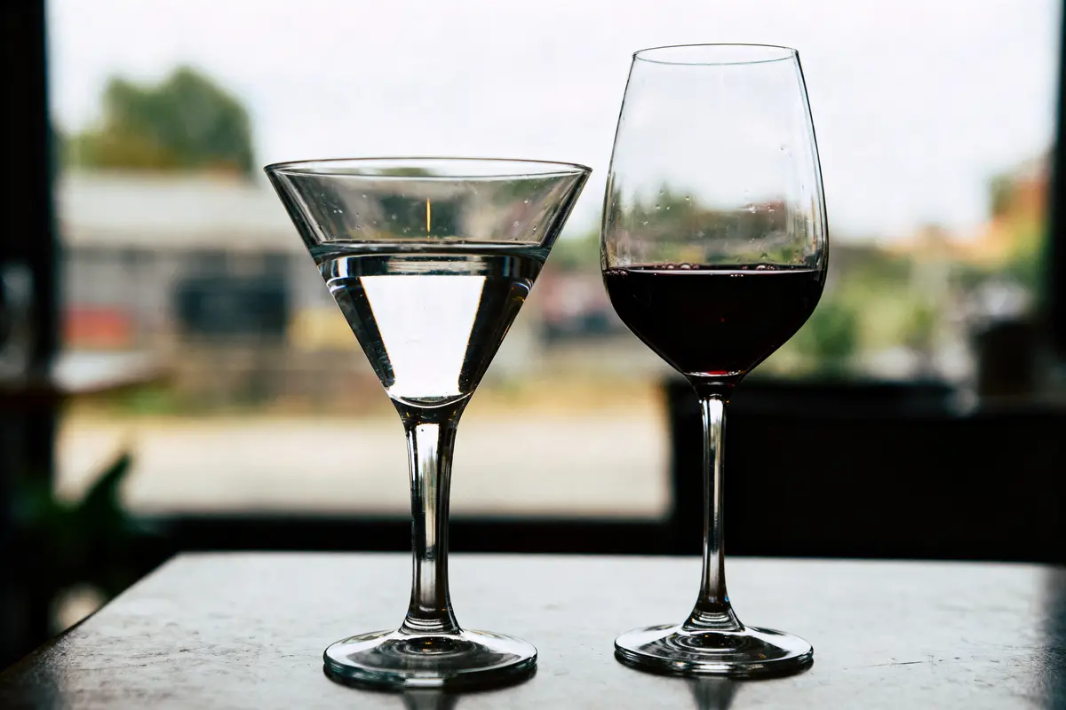Verre de cocktail clair à gauche, verre de vin rouge à droite, posés sur table intérieure.
