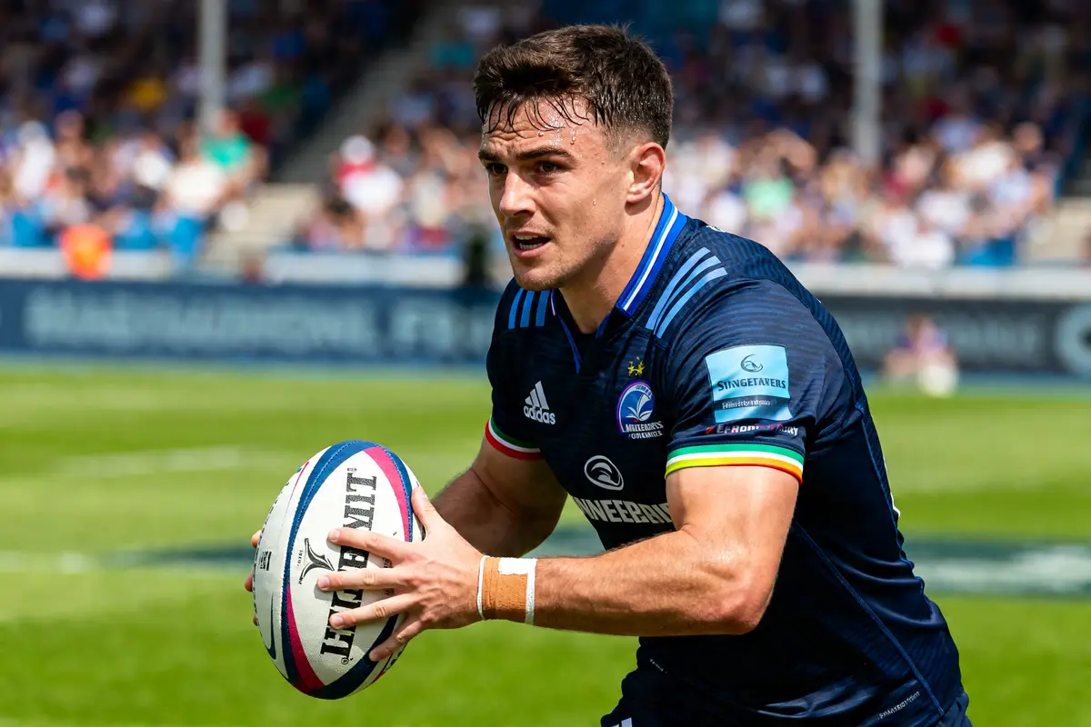 Joueur de rugby concentré avec ballon, maillot bleu et logo Sexton visible
